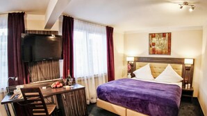 A hotel room with a bed, a desk, a television, and a painting on the wall. - Hotel Famosa (Düsseldorf)