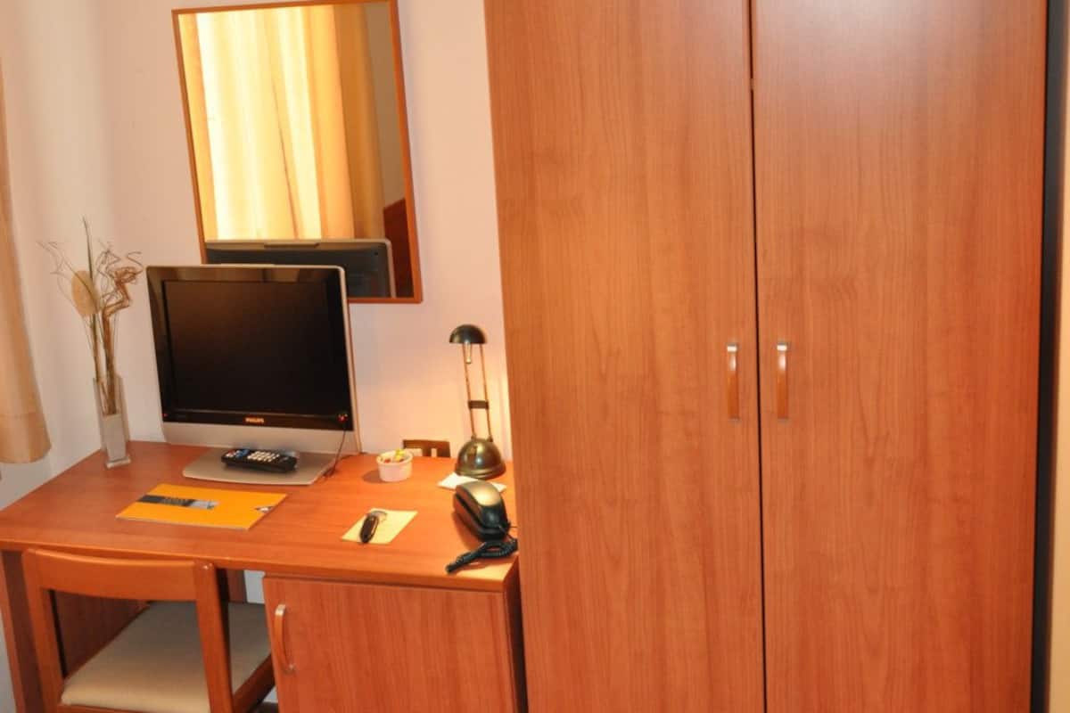 A small room with a wooden desk, a television, a mirror, and a wardrobe.