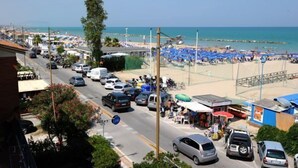 Una calle concurrida que lleva a una playa, con coches estacionados y sombrillas de playa.