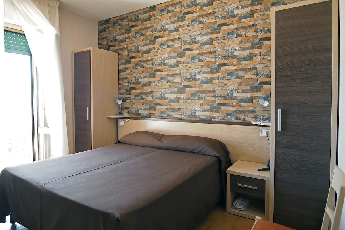 A bedroom with a bed, bedside tables, a wardrobe, and a brick-patterned wall.