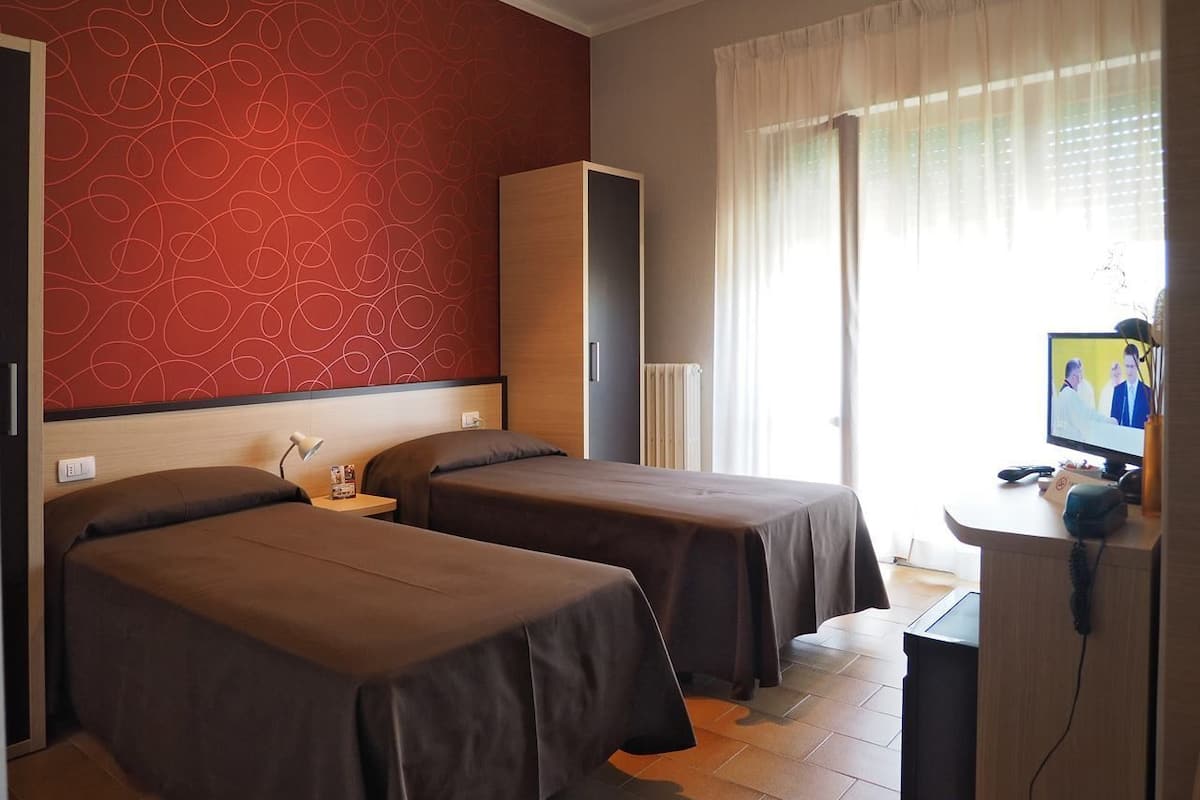 A hotel room with two beds, a desk with a computer, a TV, and a minibar.