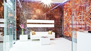 A modern interior with a white sofa, a glass partition, and a marble wall with a light fixture. - Style Hotel (Milan)