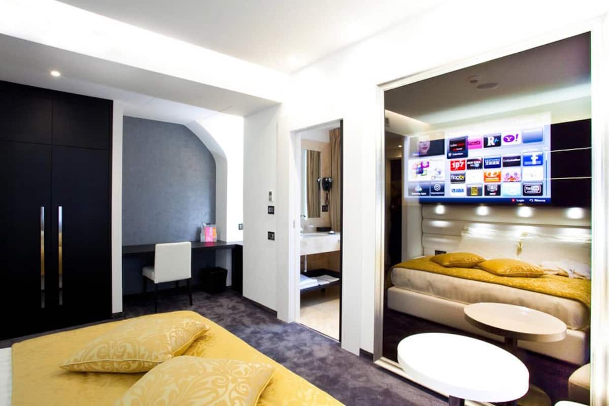 Una habitación de hotel moderna con una cama, un escritorio, un tocador y un televisor que muestra varios canales.