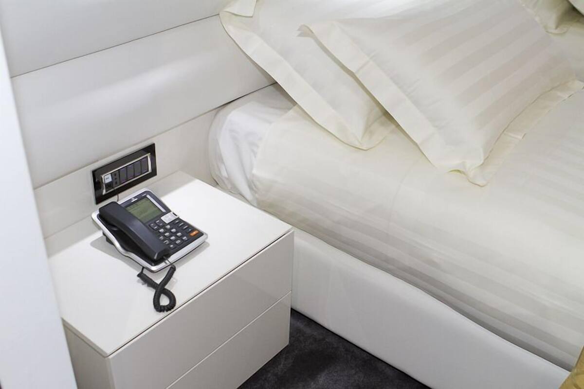 Habitación de hotel con una mesita de noche blanca, un teléfono negro y una cama bien hecha con sábanas blancas.