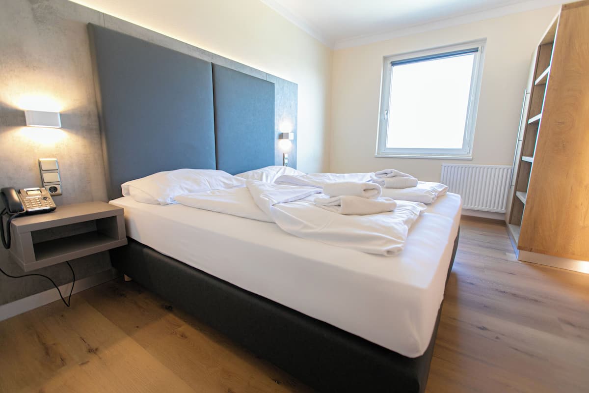 A hotel room with a bed, bedside table, lamp, and a window.