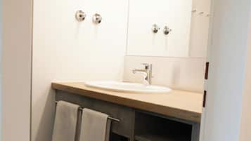 A bathroom with a sink, mirror, towel rack, and dark tiles.