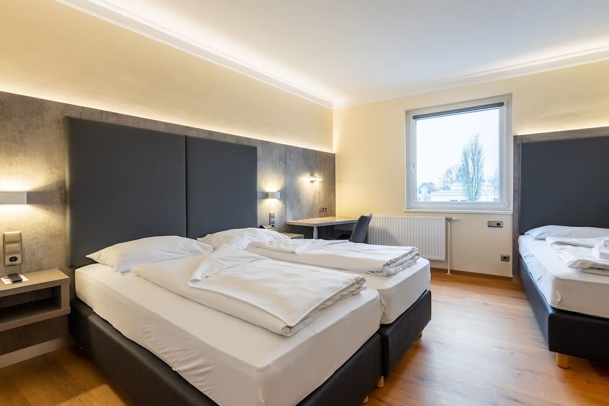 A modern hotel room with two beds, a desk, and a large window.