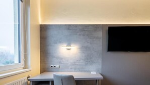 Una habitación moderna con escritorio, silla, televisor montado y ventana.