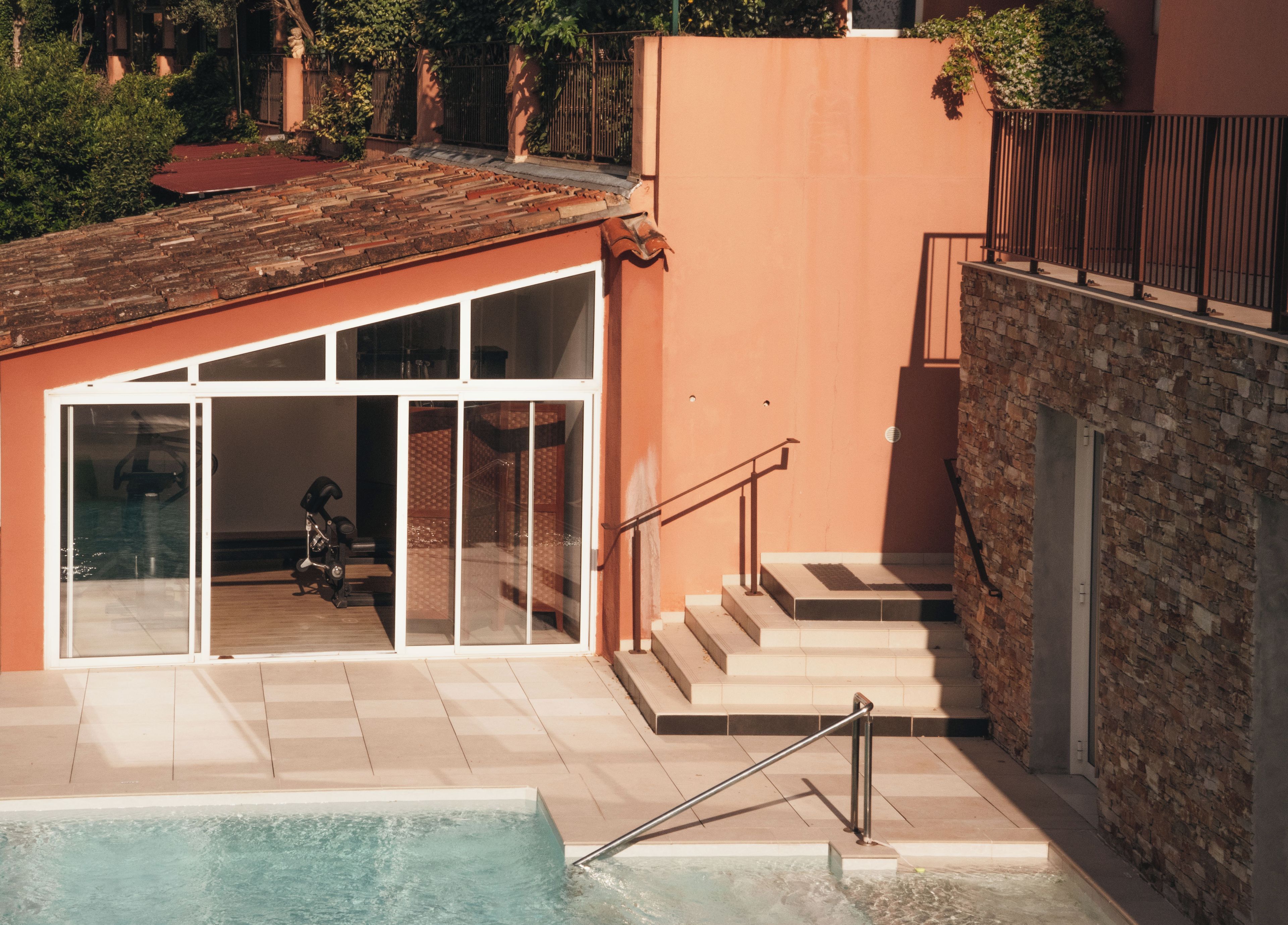 A pool area with a glass-enclosed room, a staircase, and a brick wall.