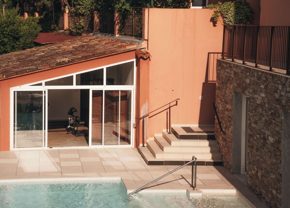 A pool area with a glass-enclosed room, a staircase, and a brick wall.