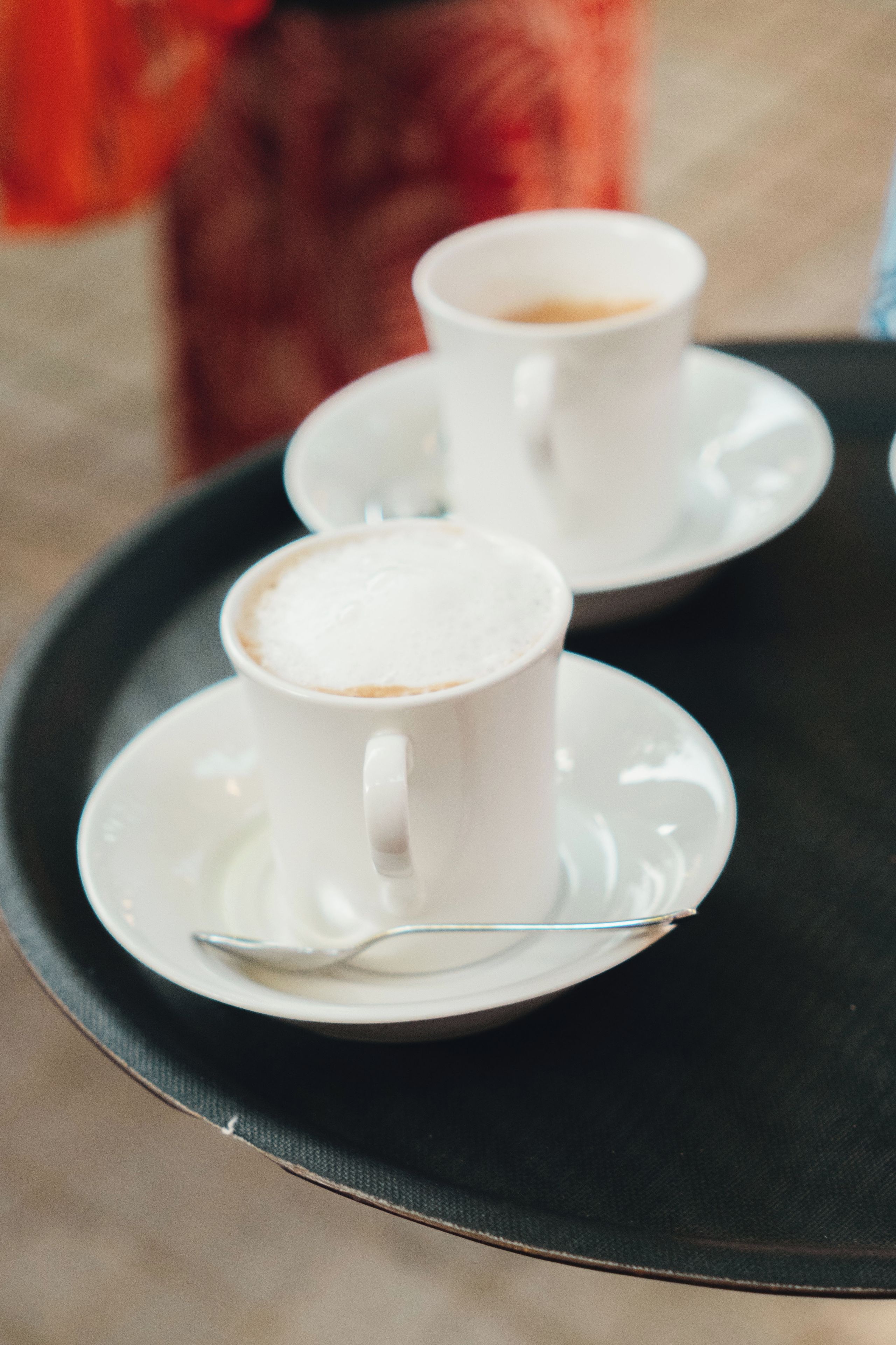 Two white cups of coffee on saucers on a black tray.