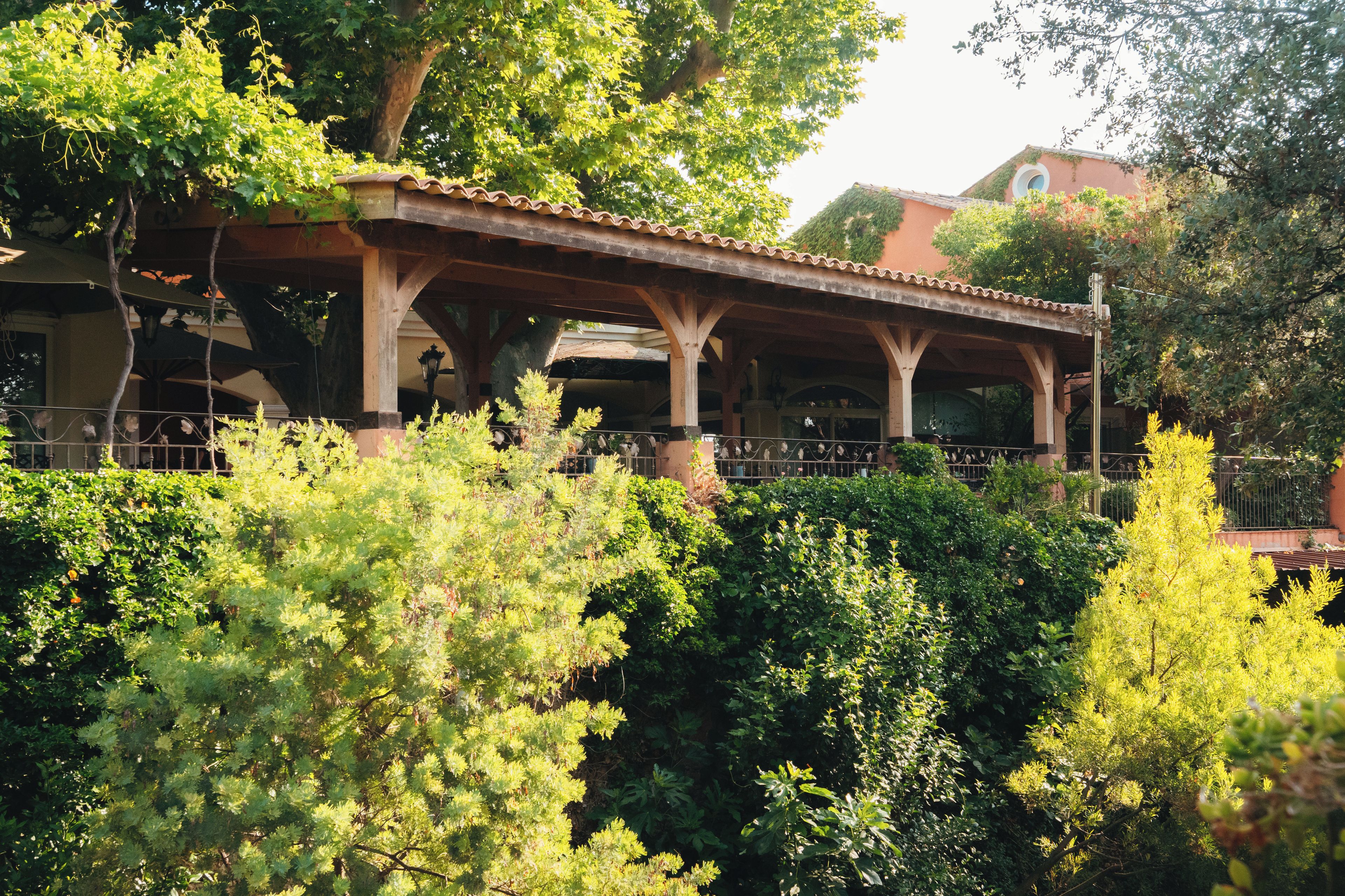 A covered outdoor area with a wooden structure, surrounded by dense greenery.