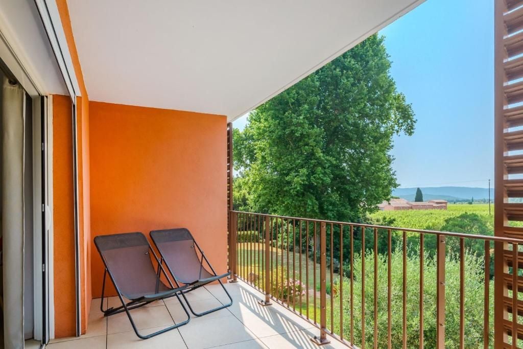 A balcony with two chairs, a view of a tree, and a distant building.