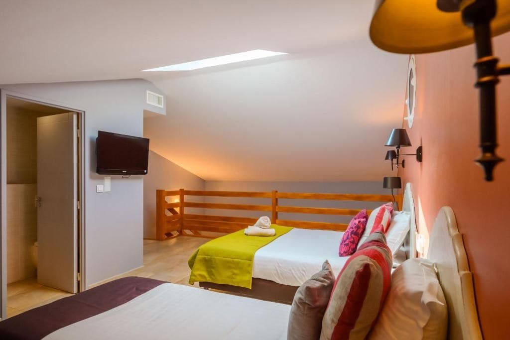 A bedroom with two beds, a television mounted on the wall, and a wooden headboard.