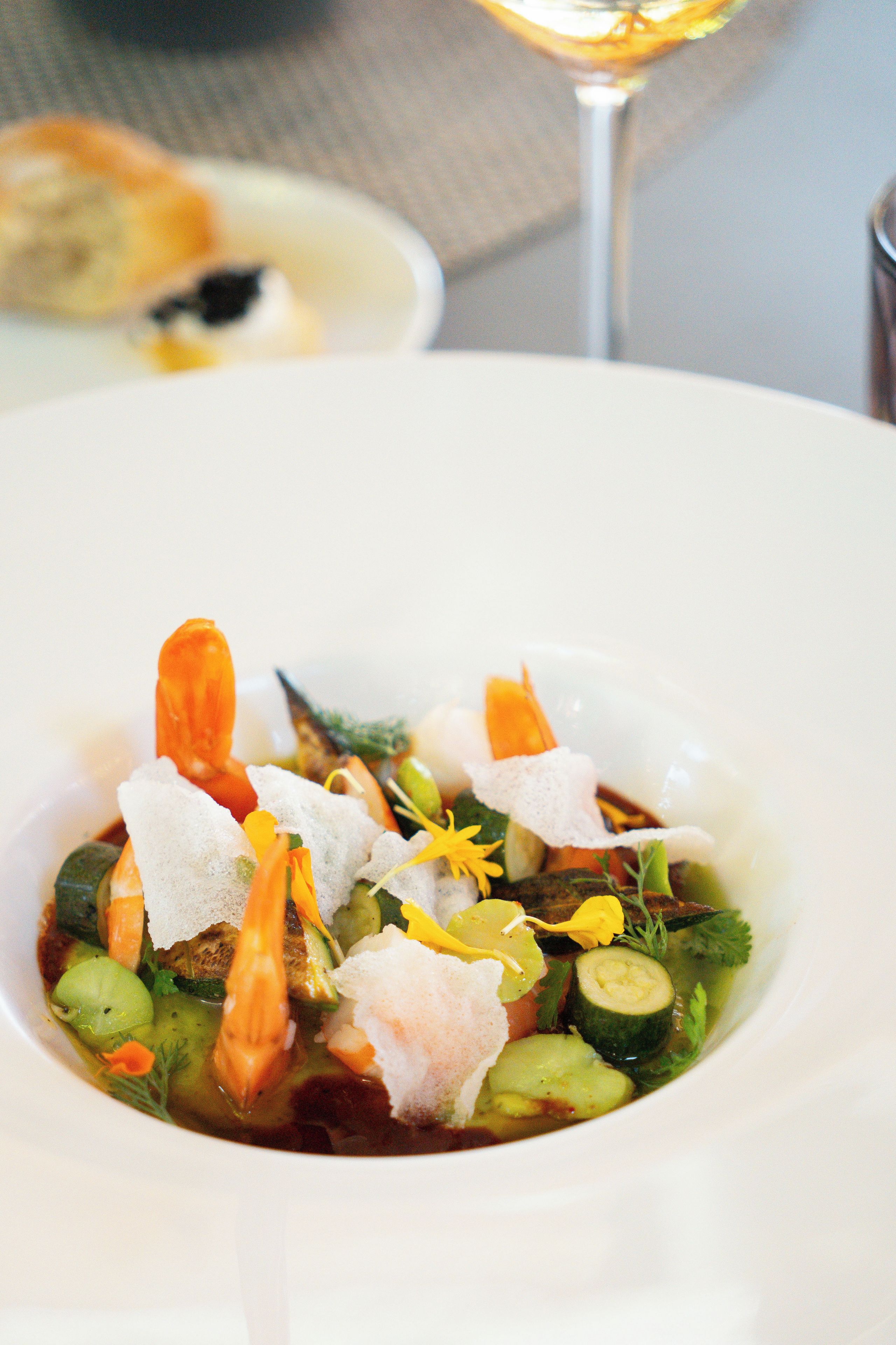 A bowl of seafood soup with vegetables and herbs.