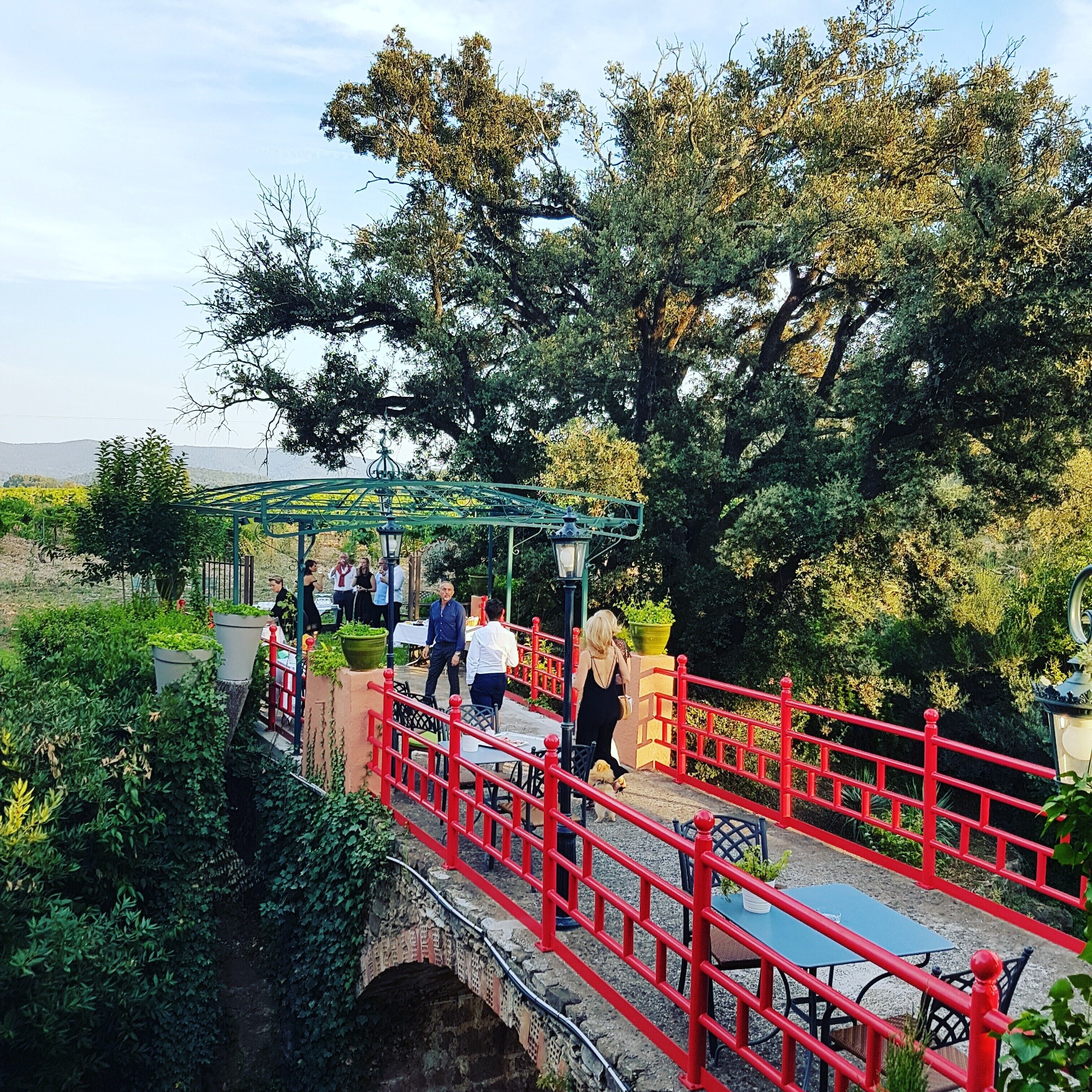 A red bridge with a covered walkway, surrounded by greenery and trees.