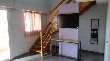 Une pièce avec un escalier en bois, un téléviseur à écran plat fixé au mur, une petite table et une fenêtre avec des rideaux.