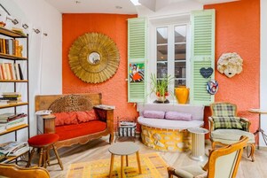 Una habitación con sofá, una mesita, una estantería y una ventana con contraventanas.