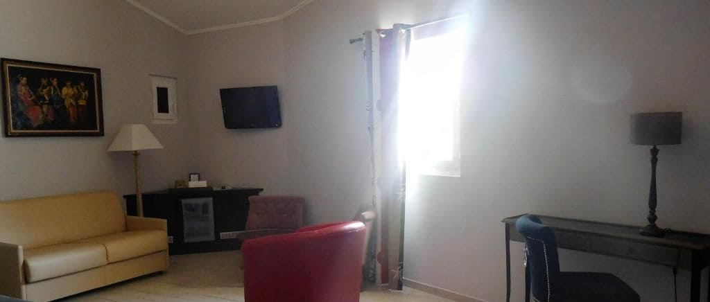 Un salon avec un canapé, un fauteuil rouge, une télévision, une lampe et une fenêtre avec des rideaux.