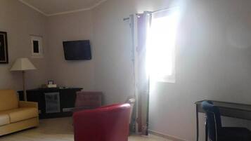 Un salon avec un canapé, un fauteuil rouge, une télévision, une lampe et une fenêtre avec des rideaux.