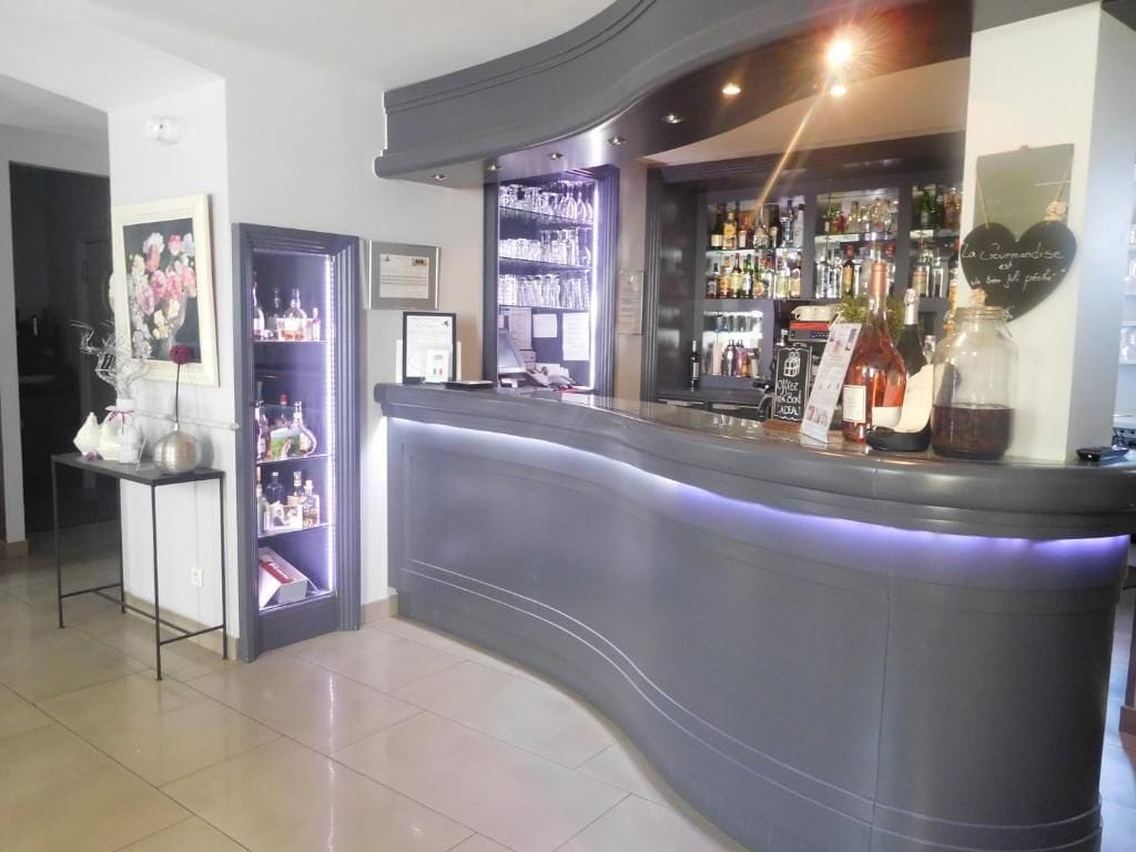 Uma área de bar com balcão curvo, prateleiras com garrafas e um letreiro decorativo em formato de coração.