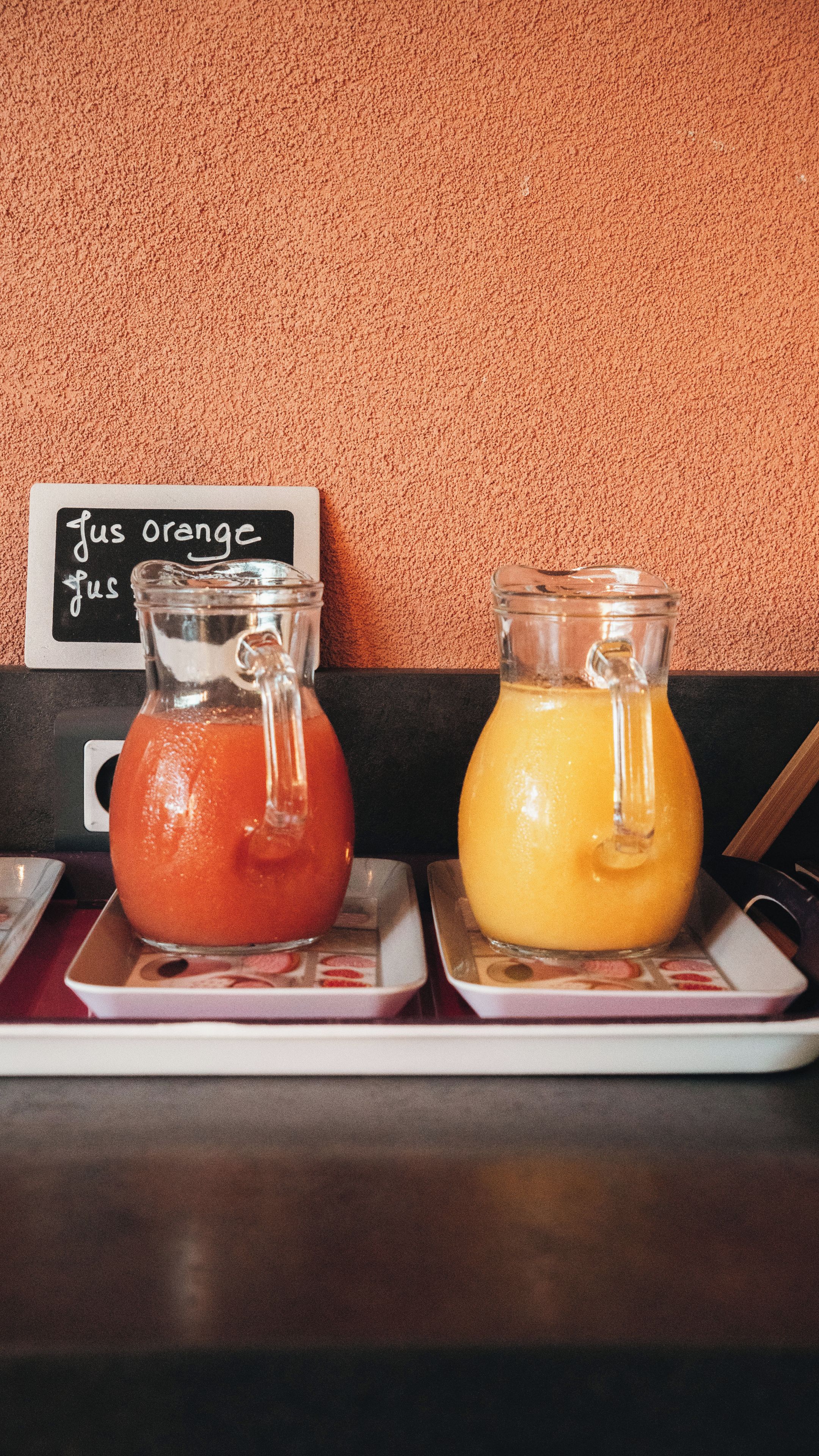 Dos vasos con jugo de naranja sobre una bandeja frente a una pared con textura.
