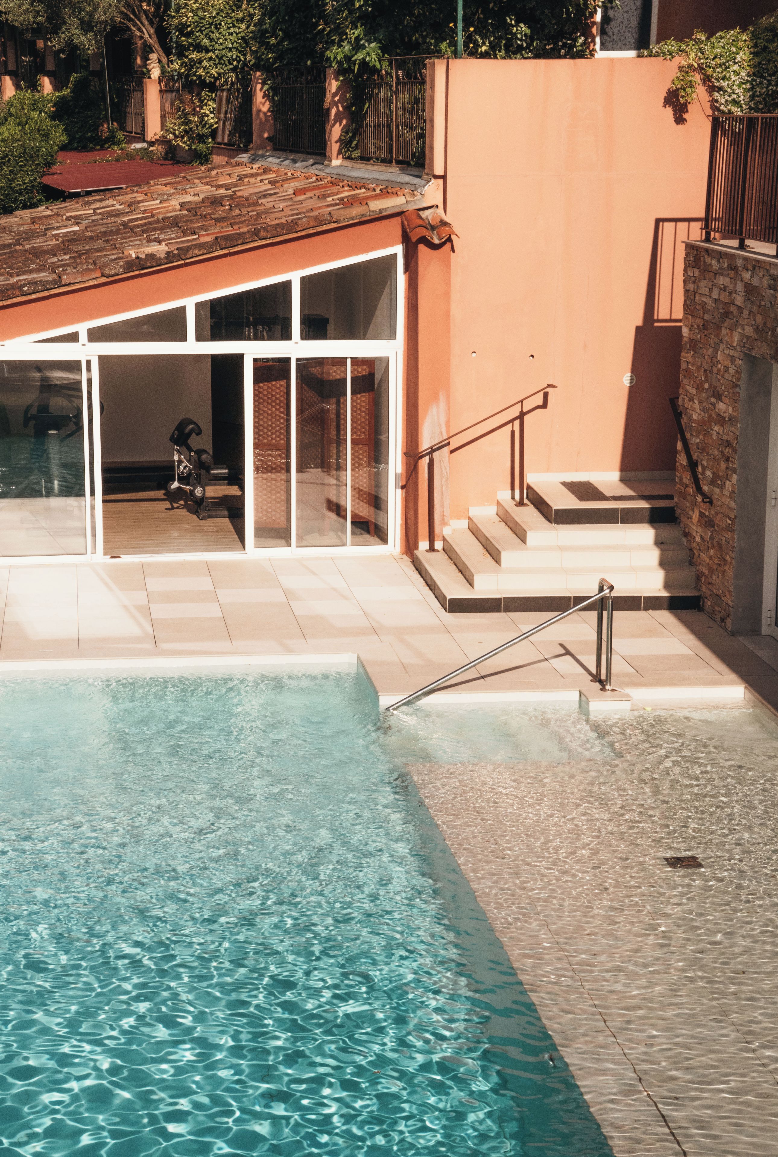 A swimming pool with clear water, a covered patio area, and a staircase leading to a higher level.