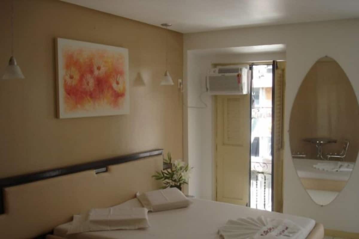 Ein Hotelzimmer mit einem Bett, einem Gemälde, einer Klimaanlage, einem Spiegel und Blick auf einen Balkon mit Gartenmöbeln.