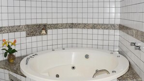 Een badkamer met een vrijstaand bad, witte betegelde wanden en een granieten aanrechtblad.