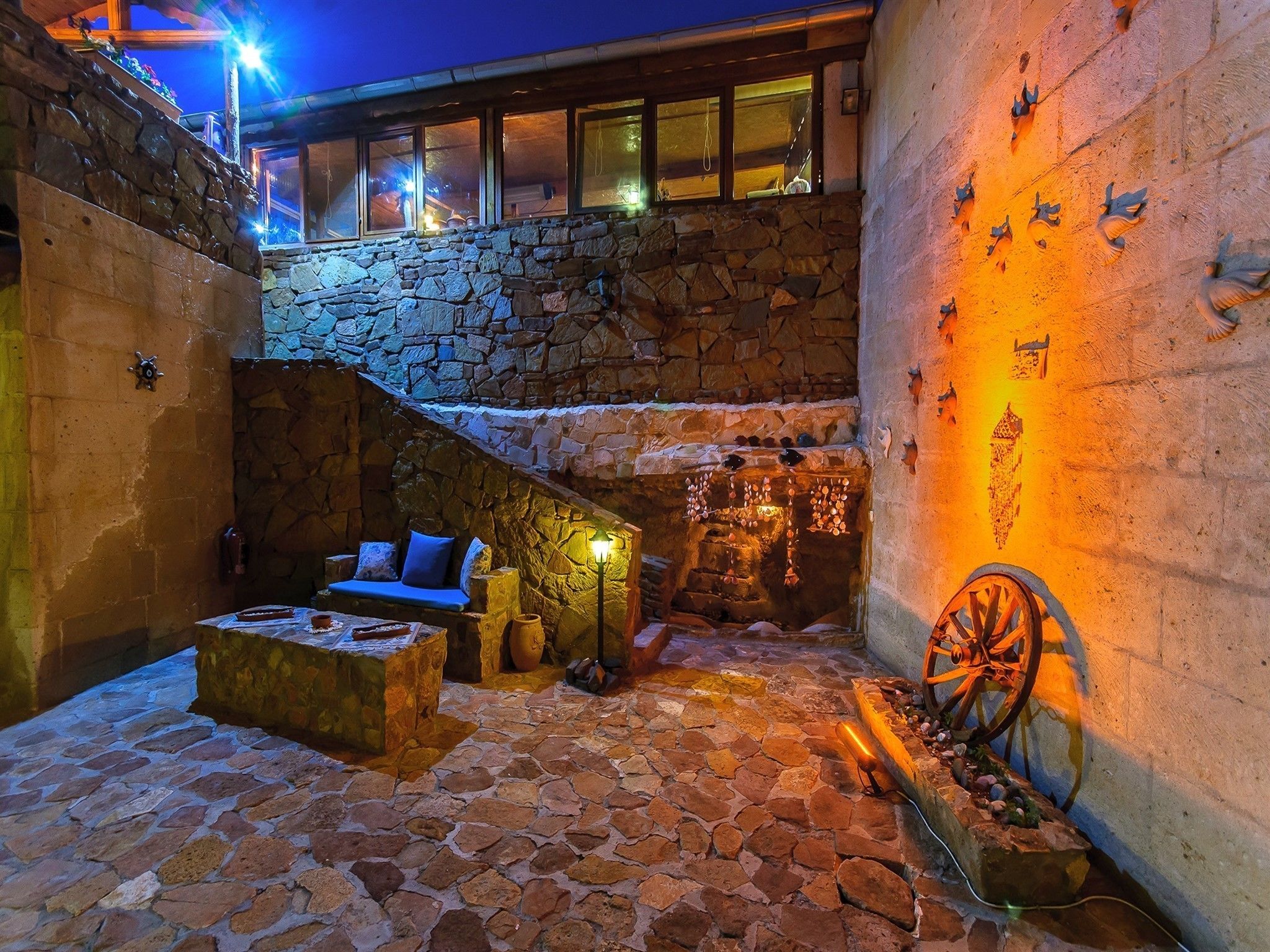 A stone courtyard with a stone bench, a small fire pit, and a decorative wheel.