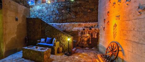 A stone courtyard with a stone bench, a small fire pit, and a decorative wheel.