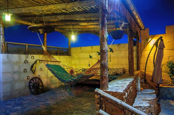 Un patio al aire libre con una hamaca, paredes de piedra y un techo de madera rústica.