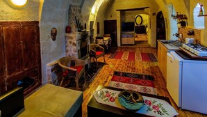 Un interior rústico con techo abovedado de piedra, una chimenea, una zona de comedor con mesa y sillas, y una cocina con estufa.
