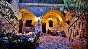 Un patio de piedra con una mesa y sillas, arcos y una escalera.