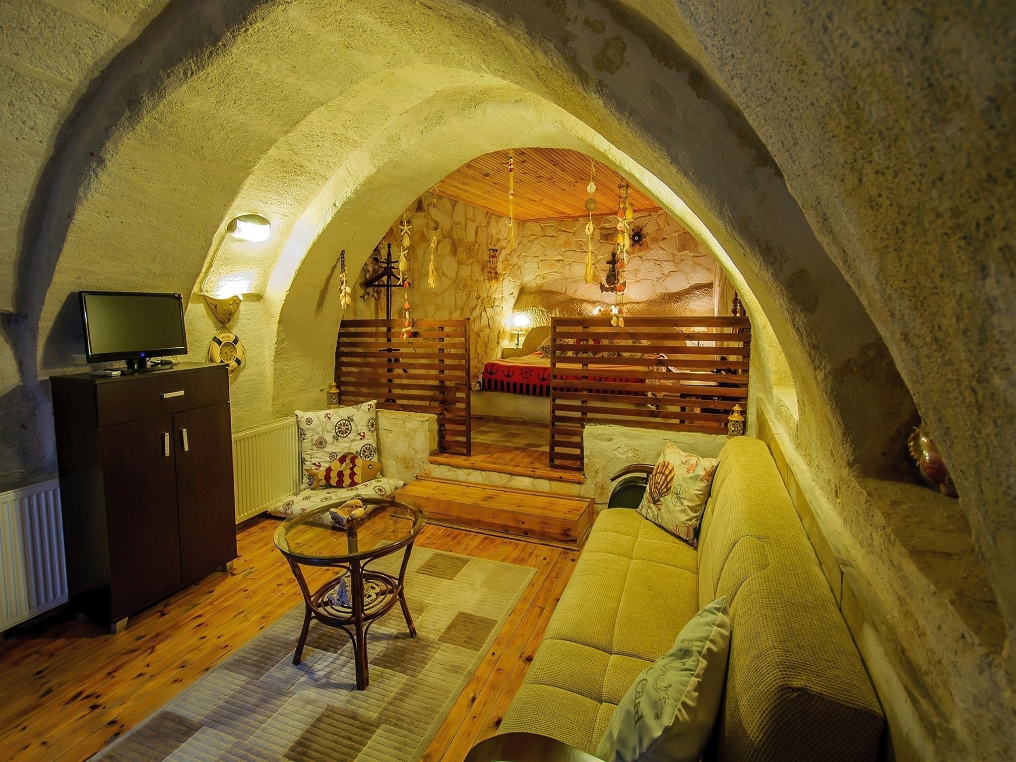 A cozy, rustic room with a vaulted ceiling, a wooden bench, a sofa, a small table, and a television on a cabinet.