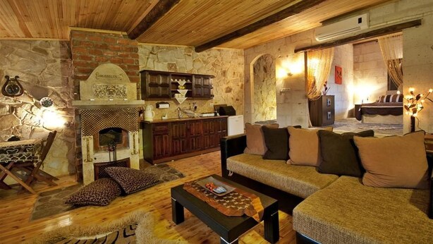 Un interior rústico con chimenea de piedra, vigas de madera, un sofá con cojines y un comedor.