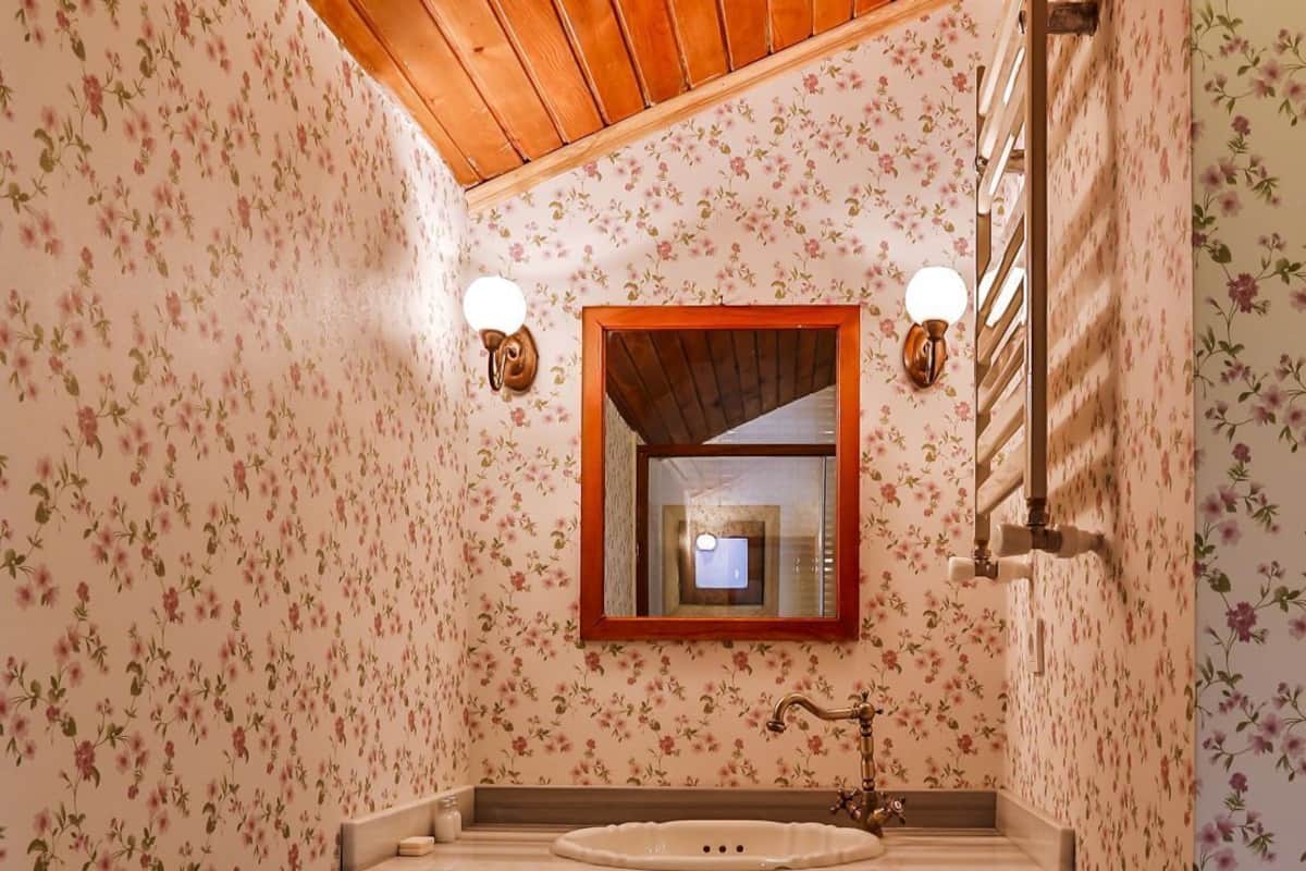 A bathroom with wooden ceiling, floral wallpaper, a wooden vanity, and a mirror.