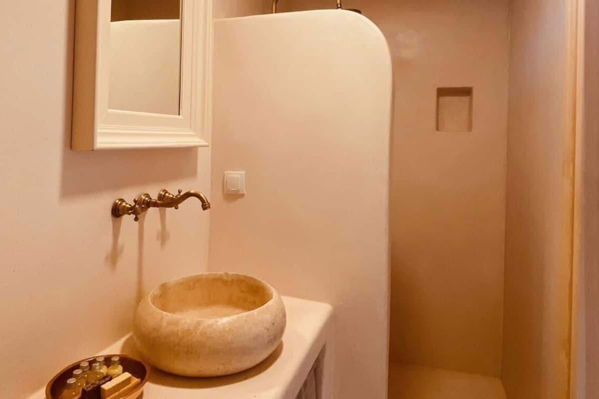 A bathroom with a wooden ceiling, a white sink, a mirror, a clock, and a shower.