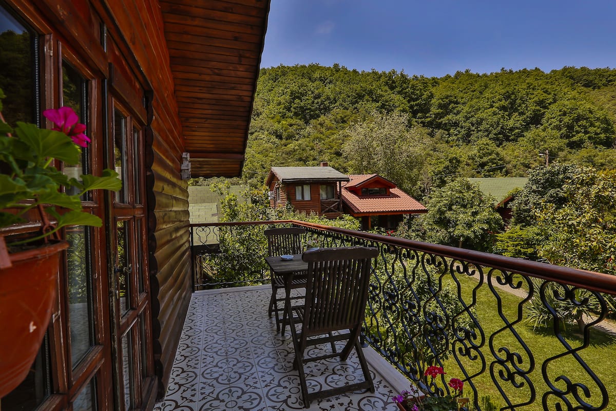 A wooden cabin with a balcony featuring a patterned floor, a table, and two chairs.