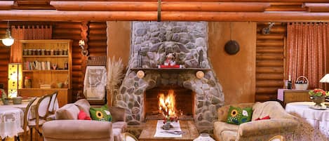 Interior acogedor de una cabaña de troncos con chimenea de piedra, muebles de madera y un comedor.