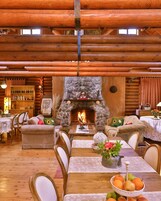 A cozy log cabin interior with a stone fireplace, wooden furniture, and a dining area.