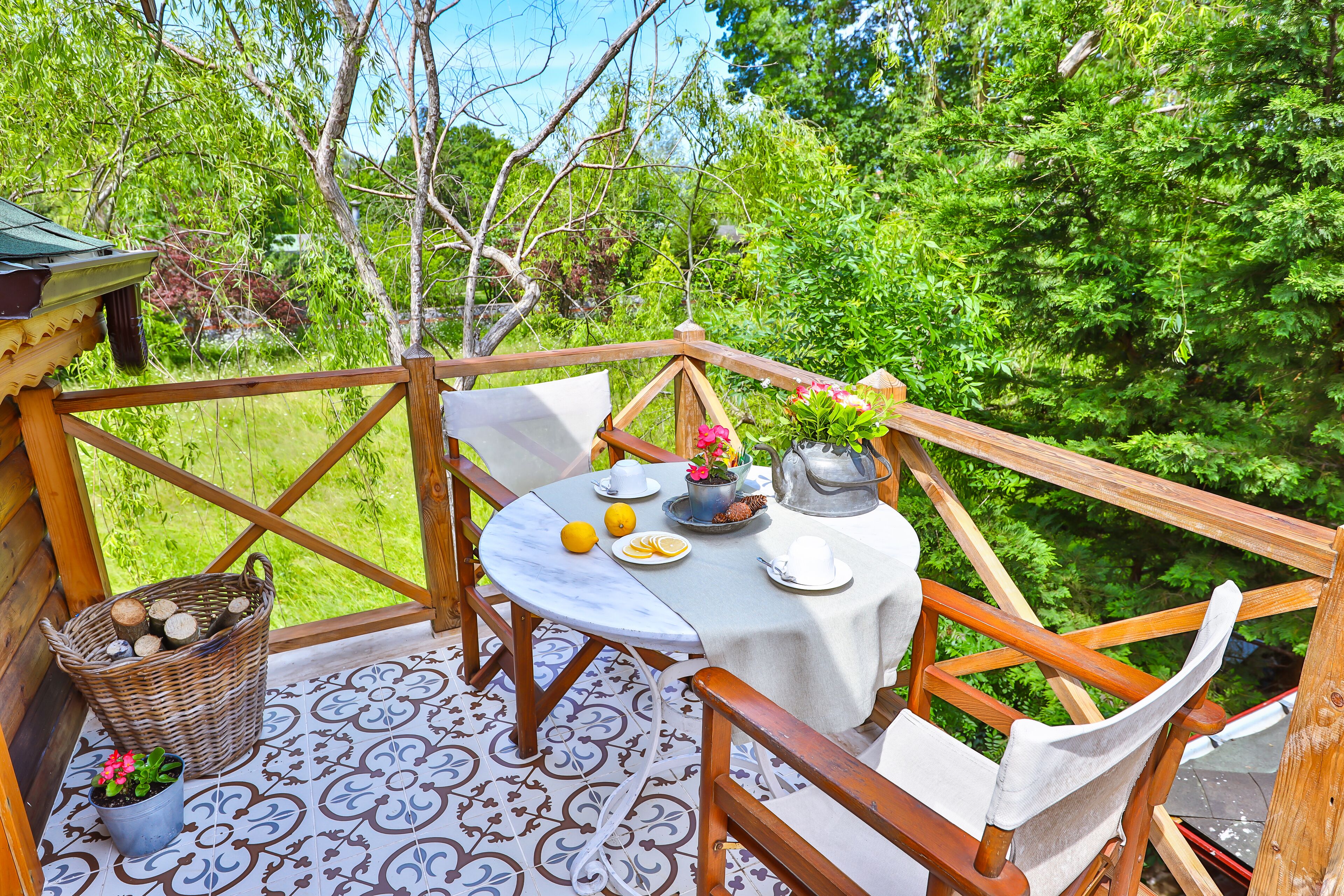 A wooden deck with a table set for two, surrounded by chairs, and a wicker basket with logs.