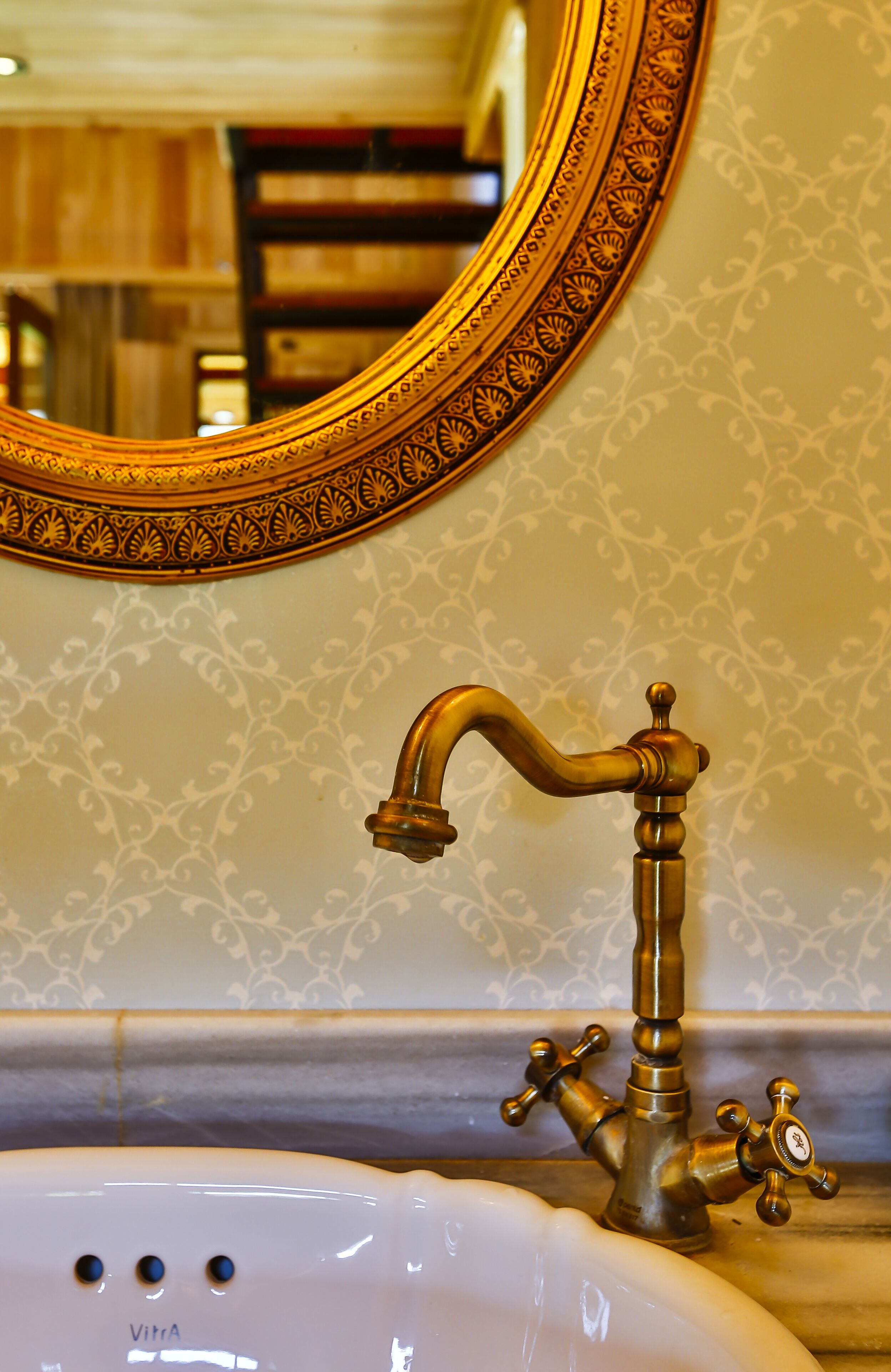 A bathroom with a white sink, a brass faucet, and a decorative mirror with an ornate frame.