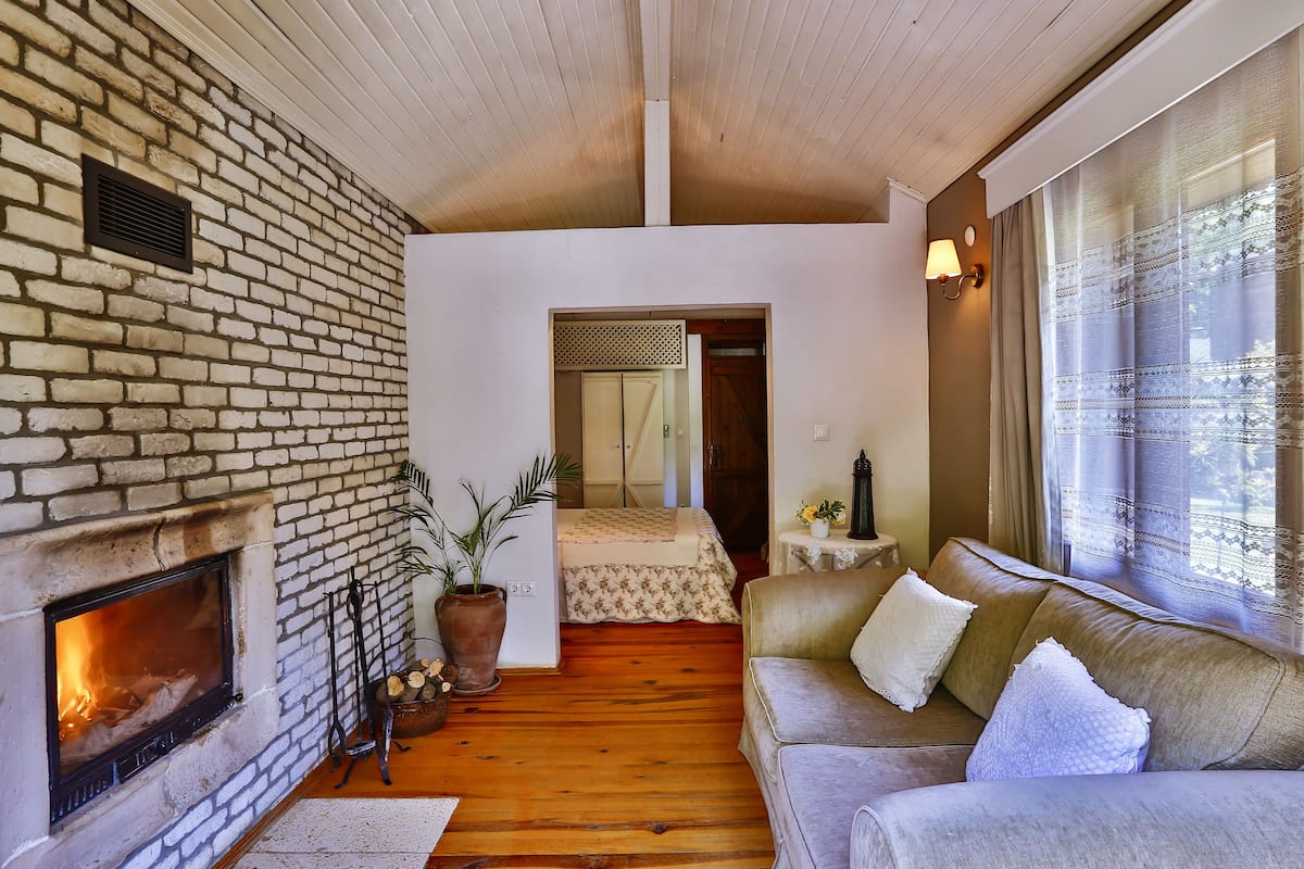 A cozy living room with a fireplace, a sofa, and a large window with curtains.