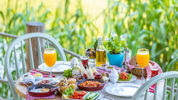Une table de petit-déjeuner installée à l’extérieur, avec différents plats, boissons et une vue sur la verdure.