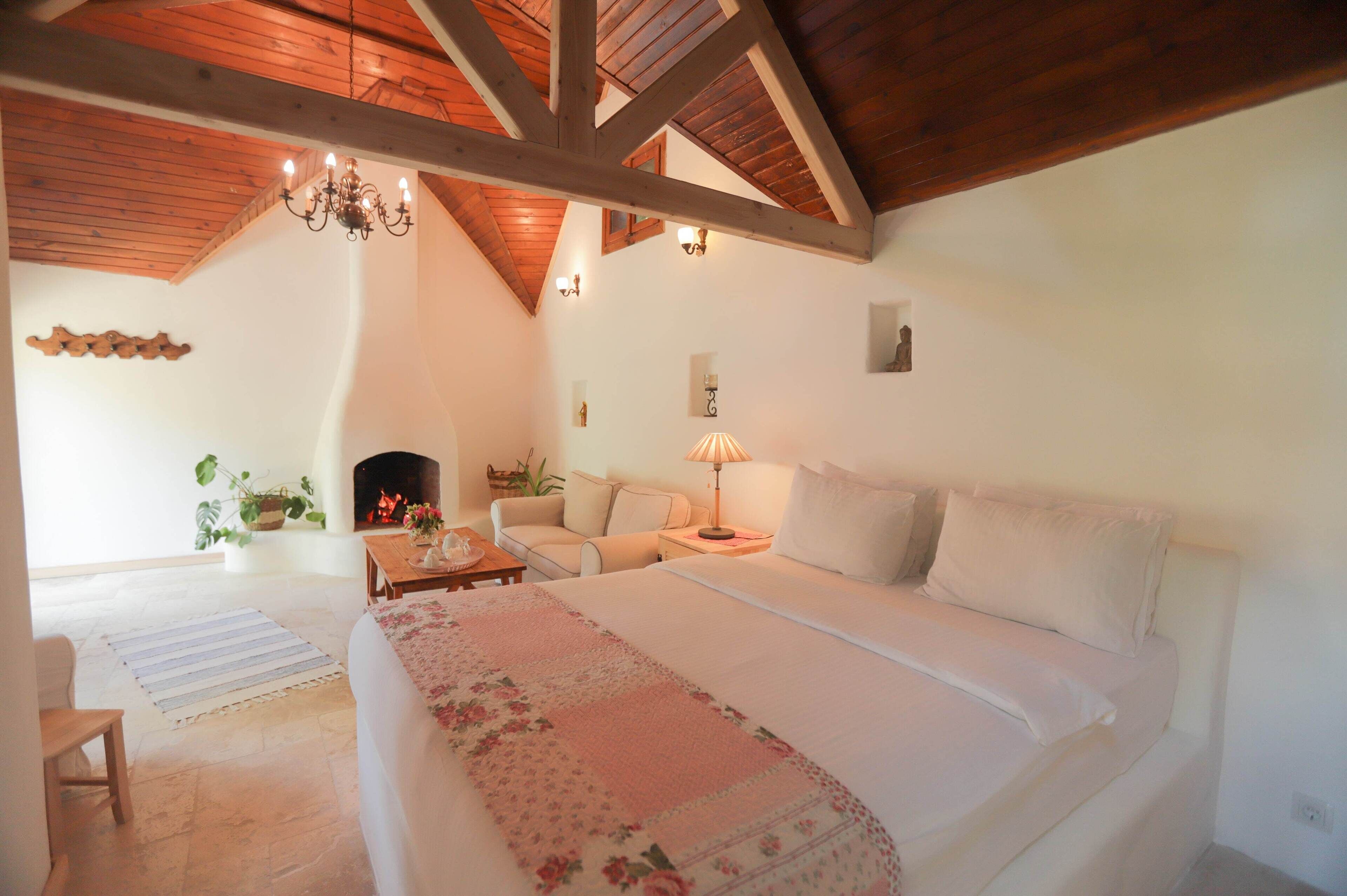 Un dormitorio con una cama grande, techo de madera, chimenea y un sofá.