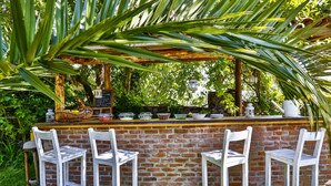 A rustic outdoor bar with a brick wall, white bar stools, and a wooden canopy. - Tranquilla River Lodge - Adults Only (Sile)