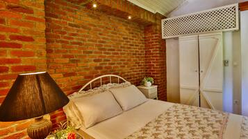Un dormitorio con pared de ladrillo, una cama con colcha estampada, una lámpara y una mesita de noche con planta.