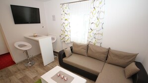 Una sala de estar moderna con sofá, mesa de centro, televisor y pequeña zona de kitchenette.