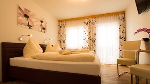 Un dormitorio con cama, una silla, un escritorio, un televisor y una ventana con cortinas.